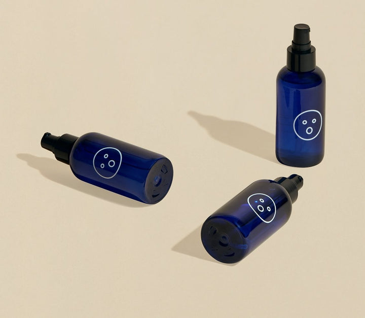 Three blue bottles of Dame Alu personal lubricant lay across cream coloured surface